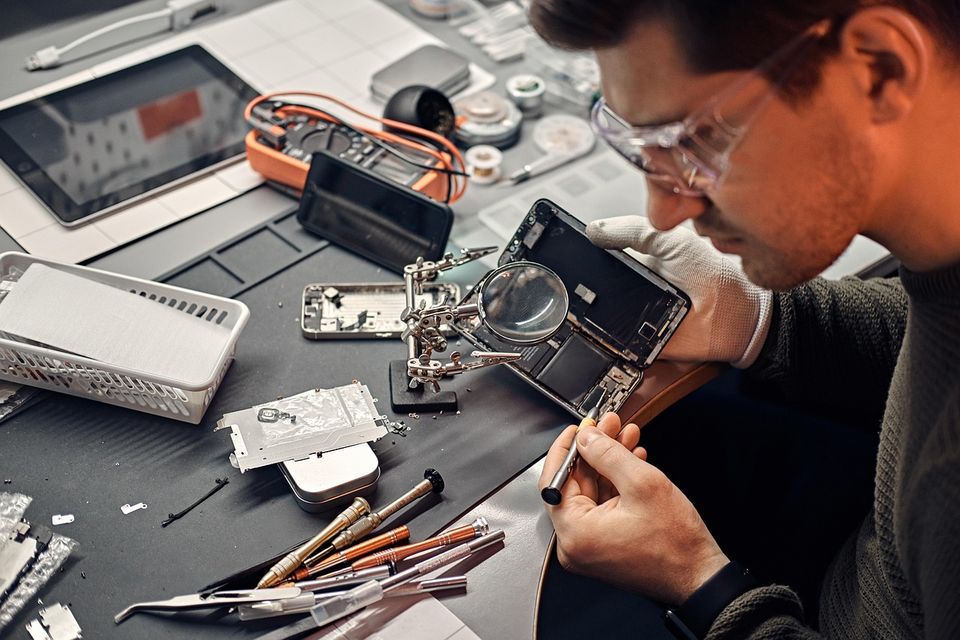 T&eacute;cnico reparando un celular con una lupa en su banco de trabajo